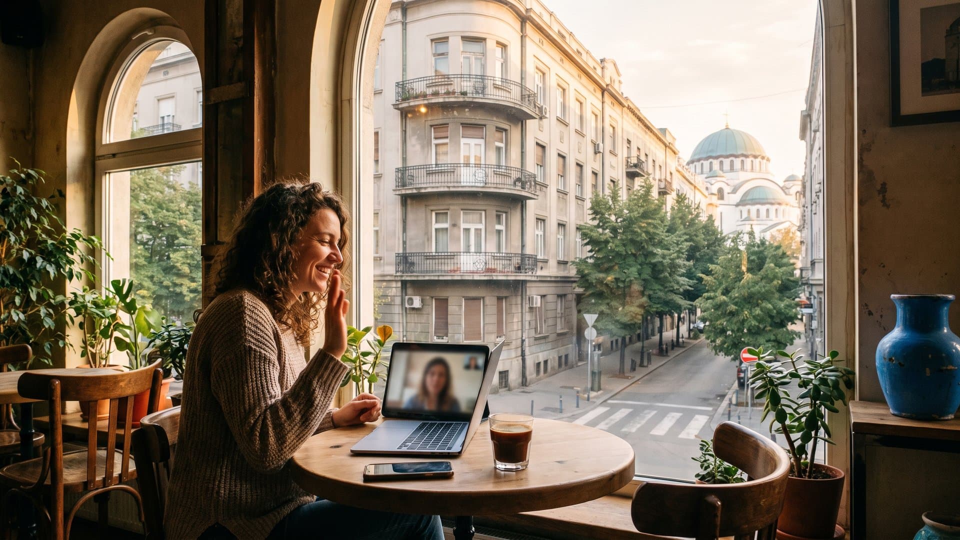 Sto pored prozora sa laptopom, telefonom i šoljom kafe